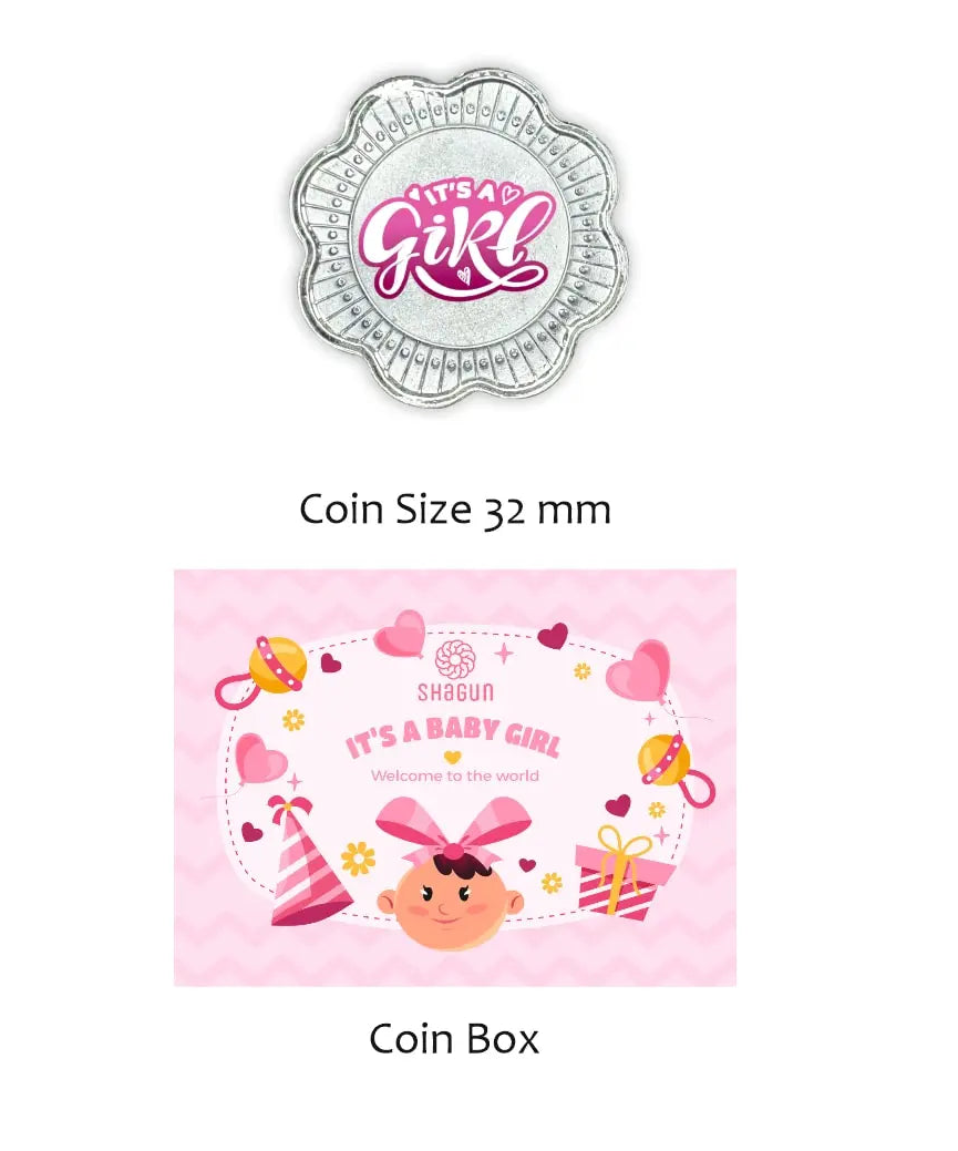 Shagun Coins baby shower themed 'It's a Girl' coin and matching coin box set. The coin is silver with pink and white lettering, and the box is pink with a cartoon baby girl illustration and baby accessories.