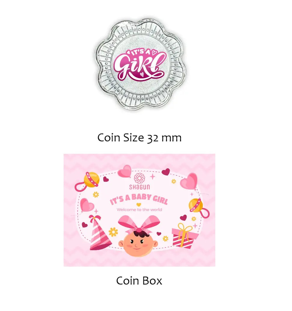 Shagun Coins baby shower themed 'It's a Girl' coin and matching coin box set. The coin is silver with pink and white lettering, and the box is pink with a cartoon baby girl illustration and baby accessories.