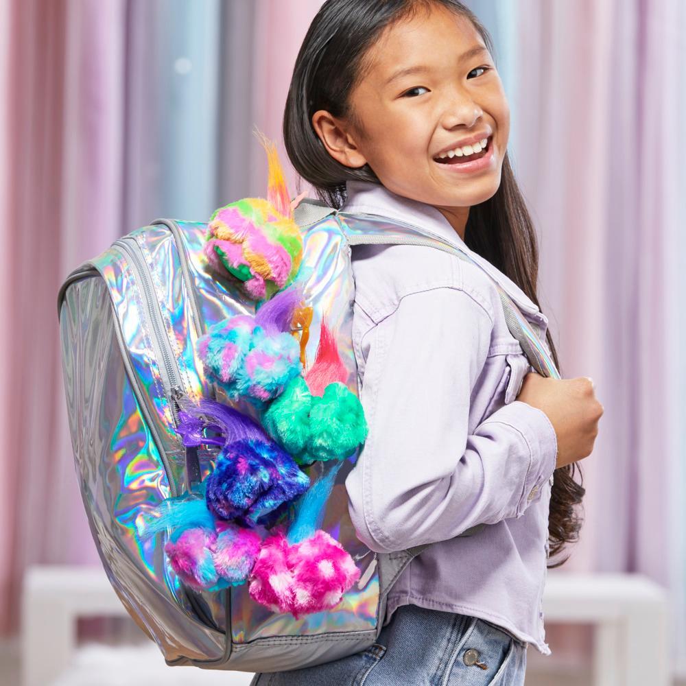Child with a colorful backpack featuring pom-poms against a light curtain background