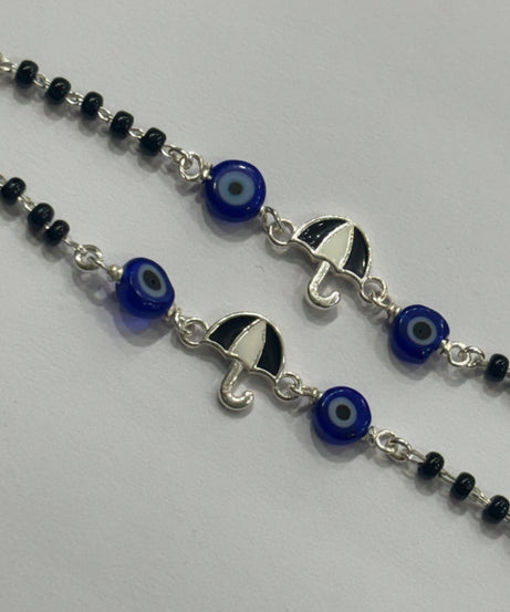 A close-up of a silver beaded necklace featuring evil eye glass beads and silver umbrella charms, laid out on a light gray background.